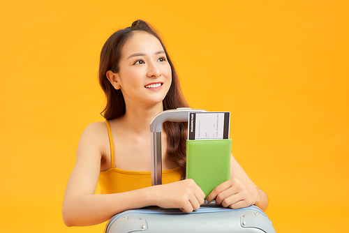 Traveler tourist woman in summer casual clothes with her passport, luggage isolated on yellow orange background.