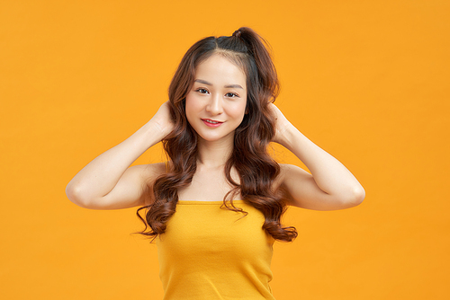 Cheerful young asian woman girl in yellow crop top posing isolated on yellow background.