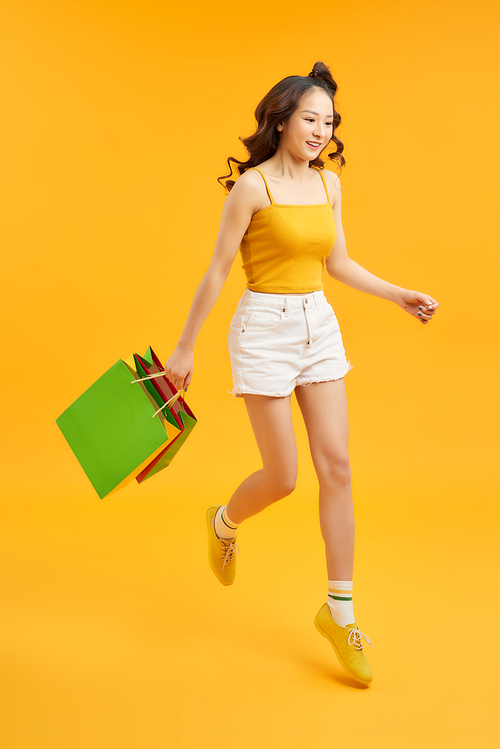 Beautiful shopaholic young woman jumping in the air with shopping bags over orange background.