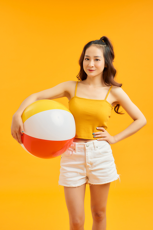 Young beautiful woman play with beach ball in summertime over orange background.