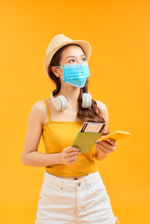 Young Asian woman holding phone, passport and wearing face mask for protection coronavirus over orange background.