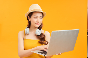 Traveler tourist woman in yellow summer clothes, headphone with laptop pc computer isolated on orange background.
