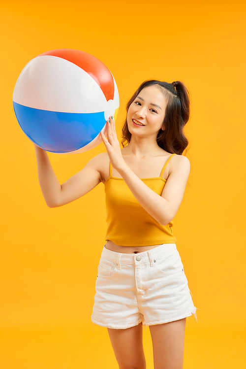 Young beautiful woman play with beach ball in summertime over orange background.
