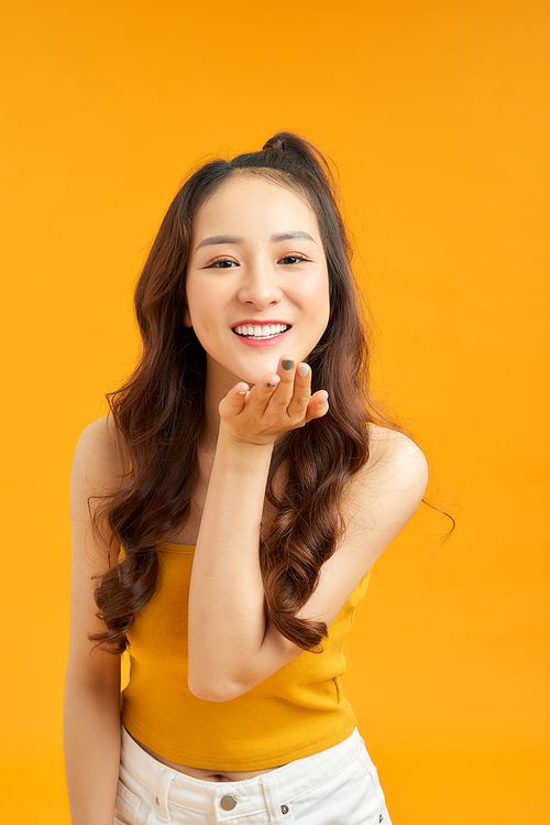 Pretty friendly girl blow camera isolated on yellow background