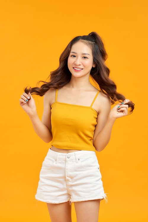 Waist up portrait of happy asian girl  smiling broadly  posing against yellow studio wall
