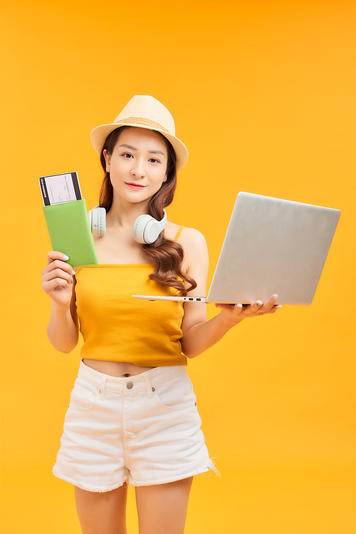 Young Asian woman holding passport and laptop over orange background.