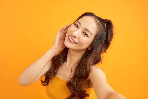 Portrait of a smiling cute woman making selfie photo on smartphone isolated on a yellow background