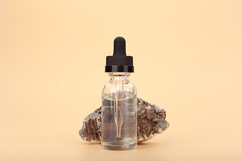 Skin serum bottle next to natural stone against bright beige background with copy space. Concept of luxury skin serum or oil for anti aging daily treatment
