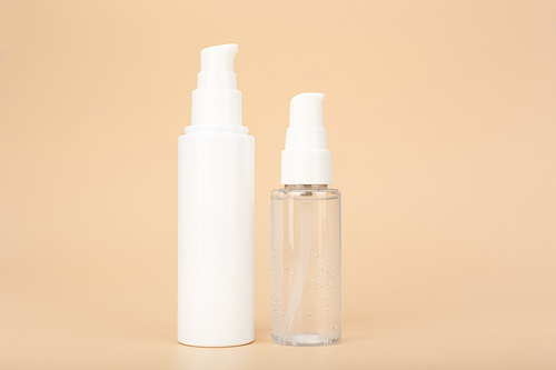 Concept of skin care and beauty products for daily skin care. Transparent bottle with liquid face gel or foam and skin cream or lotion against bright beige background with copy space
