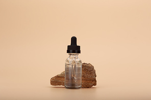 Skin serum bottle next to natural stone against bright beige background with copy space. Concept of luxury skin serum or oil for anti aging daily treatment