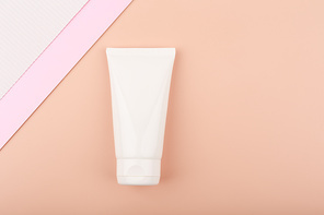 Creative elegant flat lay with white cream tube with face or hand cream or lotion on bright pastel beige background decorated with white and pink paper. Concept of beauty products for skin care