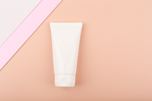 Creative elegant flat lay with white cream tube with face or hand cream or lotion on bright pastel beige background decorated with white and pink paper. Concept of beauty products for skin care
