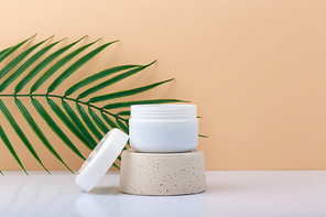 White opened cosmetic jar on gypsum podium against pastel beige background with copy space. Concept of organic natural skin care products with nourishing, moisturizing or anti aging effect
