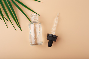 Simple elegant flat lay with opened skin serum or oil bottle on pastel beige background with palm leaf. Concept of anti aging or luxury skin treatment