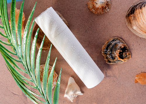 a white tube for  cream, shaving foam, spray, shampoo with drops lying among shells  on the sand on the seaside