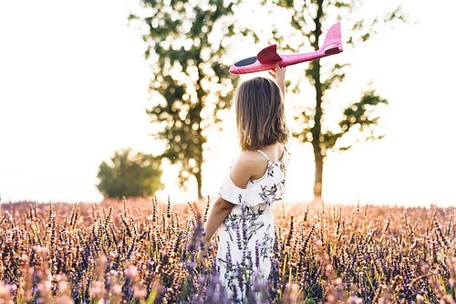 Girl with the airplane in the hands at sunset. Happy girl with a toy airplane on a lavender field in the sunset light. Children play toy airplane. Concept big child dream