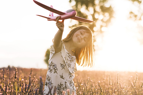 Portrait happy kid with toy airplane against summer sky background. Girl with airplane on a summer lavender field. Best childhood and big child dream concept.