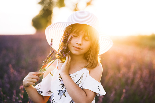 Close up portrait of young happy little girl with a hat on her head in lavender fields on the background. Woman dressed in a hat in spring time.
