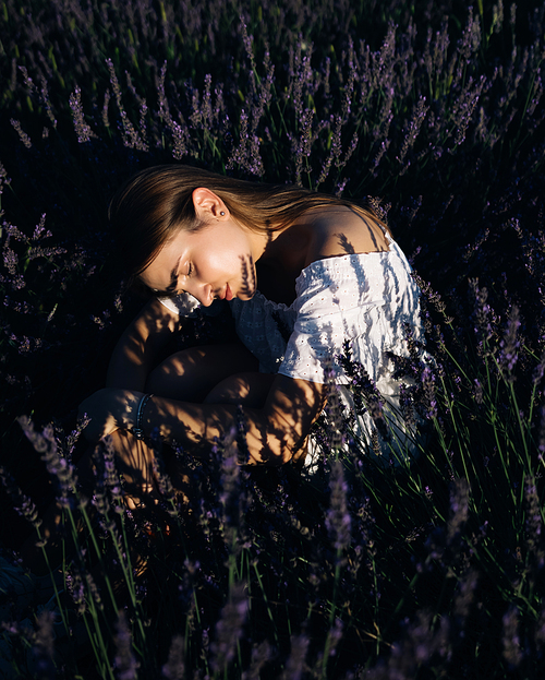 Beautiful girl in lavender field on sunset in France. Romantic woman in fairy field of lavender. Young woman in dress outdoors.