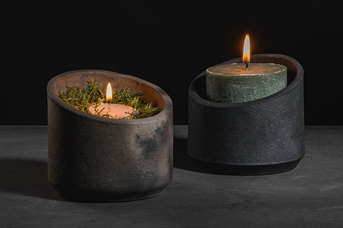 Modern design black ceramic vases  with lit candles on dark countertop and background.