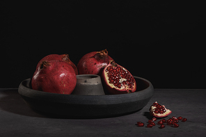 Modern design black ceramic bowl with pomegranate fruit on dark countertop and background.