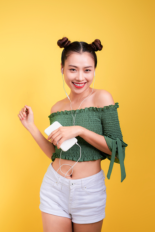 Beautiful young asian woman in headphones listening to music and singing on yellow background