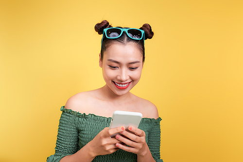 Portrait of a cheerful cute woman using smartphone isolated over yellow background