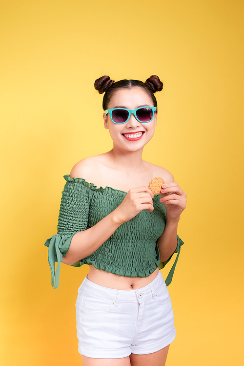 Glamor stylish beautiful young woman model with red lips holding cookie on yellow background.