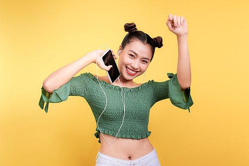 Fashion smiling asian woman listening to music in earphones  over yellow background