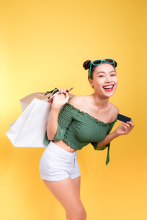 Shopping asian woman holds shopping bags and a credit card on yellow background