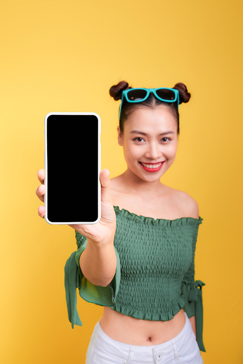Portrait of a cheerful cute woman showing blank smartphone screen isolated over yellow background