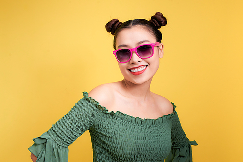 Stylish beautiful young woman in sunglasses against yellow background.