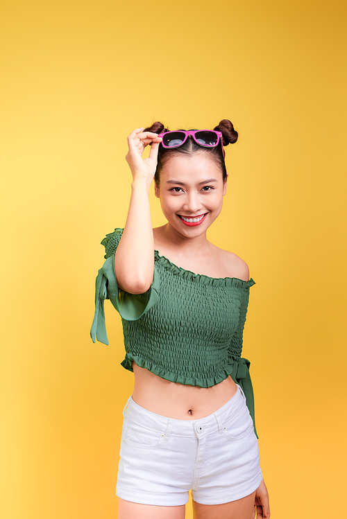 Stylish beautiful young woman in sunglasses against yellow background.