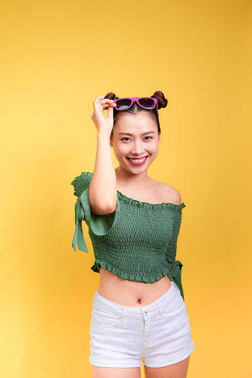 Stylish beautiful young woman in sunglasses against yellow background.