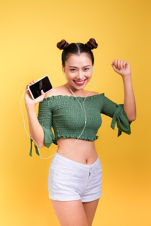 Fashion smiling asian woman listening to music in earphones  over yellow background