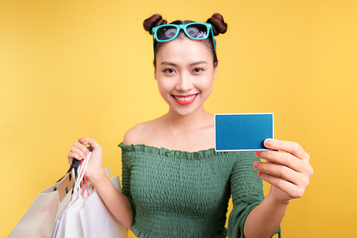 Shopping asian woman holds shopping bags and a credit card on yellow background