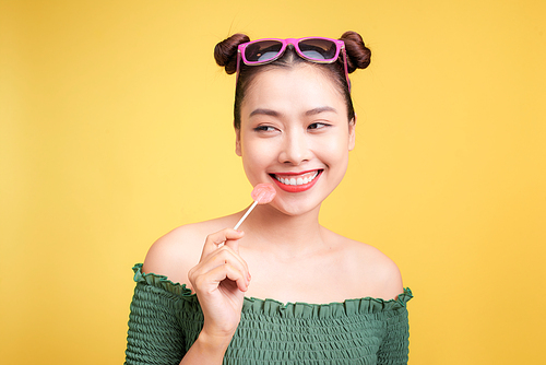 Glamor stylish beautiful young woman model with red lips holding candy on yellow background.