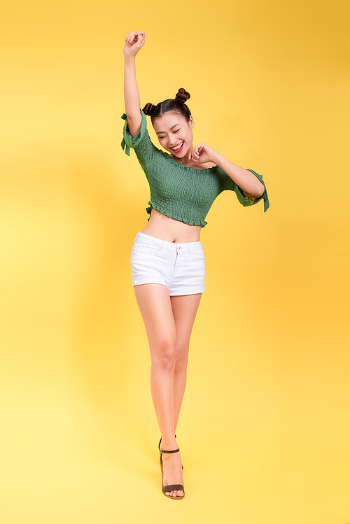 Full length portrait of beautiful young woman in sunglasses against yellow background.