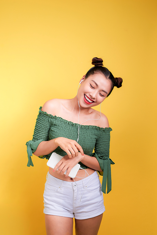 Fashion smiling asian woman listening to music in earphones  over yellow background