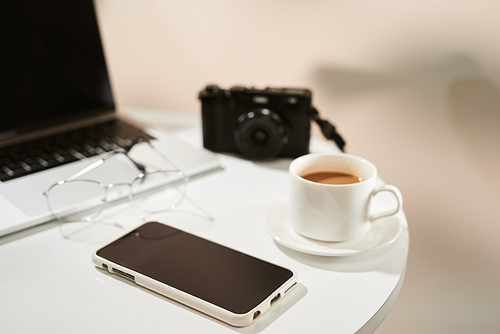 Office desk with mobile phone, coffee cup, laptop, camera and glasses