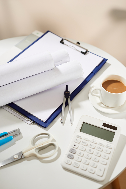 Top view of notebook, empty page, calculator, coffee cup, scissors and paper knife on white table