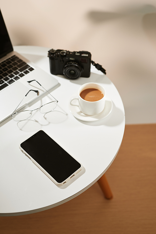 top view of office desk table with coffee cup, laptop, camera, smartphone and glasses