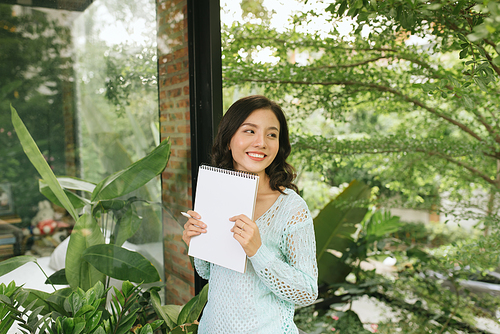 Happy Beautiful Asian Woman holding book or diary on green natural outdoor background.