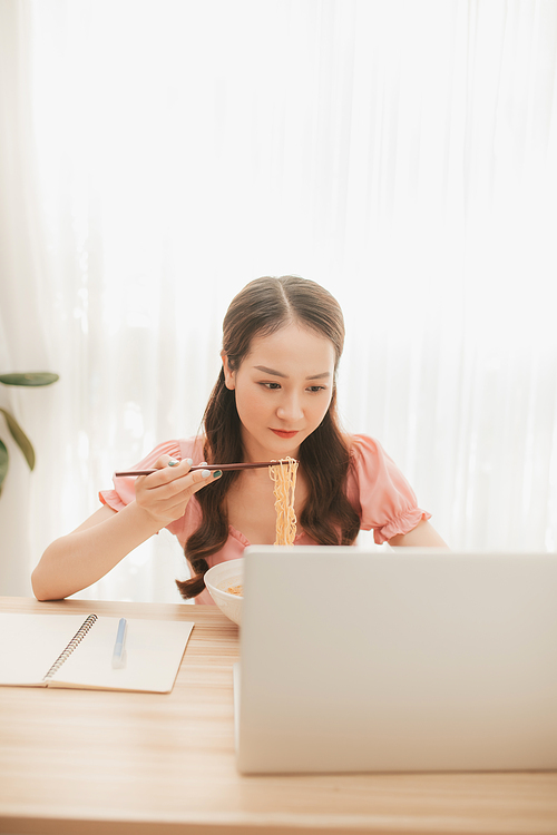 Female employee holding chopsticks eating instant noodle at workplace in home office