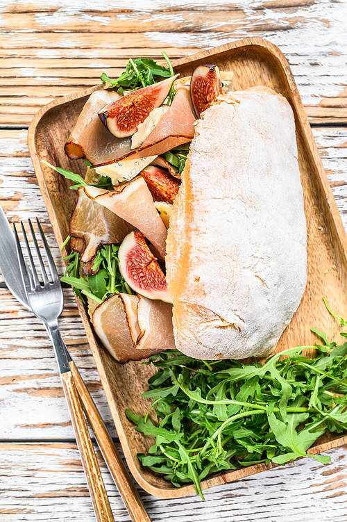 Sandwich with arugula, fig, prosciutto, Ciabatta and blue cheese on a wooden tray. White background. Top view.