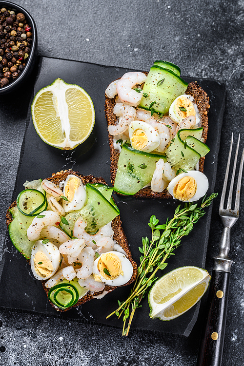 Fresh toasts with shrimp, prawns, quail eggs and cucumber on rye bread. Black background. top view.