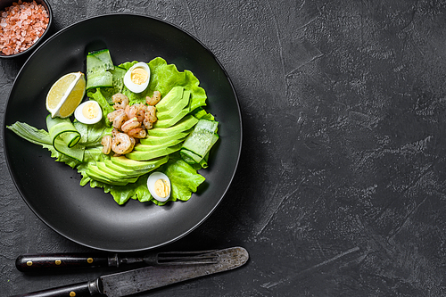 Fresh seafood salad with grilled shrimps prawns, egg, avocado and cucumber in a plate. Black background. top view. Copy space.