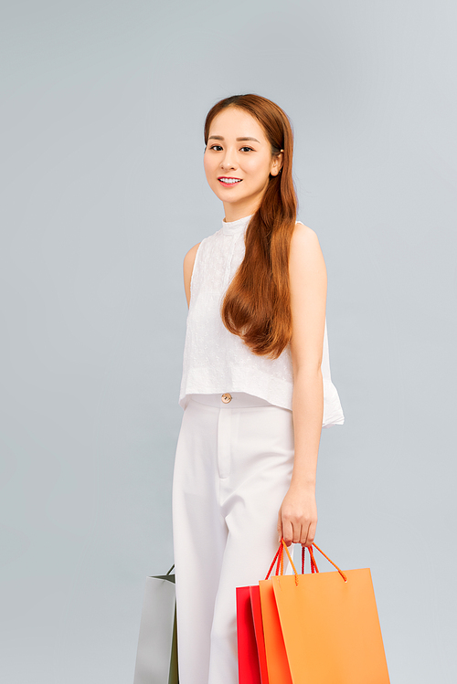 Portrait of an excited beautiful asian woman wearing dress and holding shopping bags isolated on white.