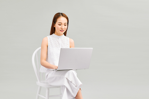 Young woman asian happy using laptop sitting on white chair isolate