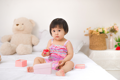 Little cute asian baby girl sitting on bed playing